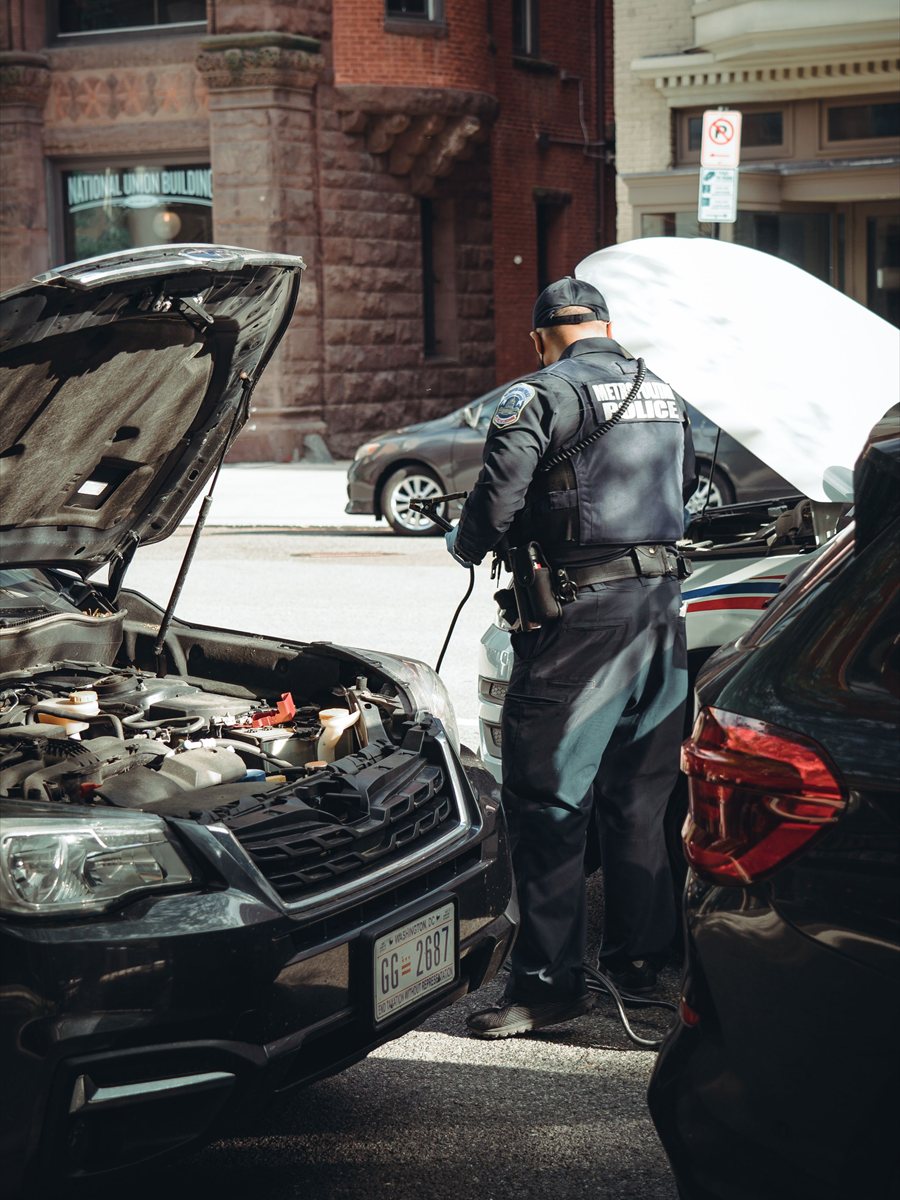 Persona conectando cables de paso a la batería de un auto estacionado en la calle